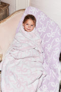 Light purple patterned teddy bow blanket with white motif, child cuddled in blanket