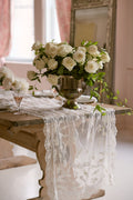 White lace table runner draped on dining table with floral centerpiece
