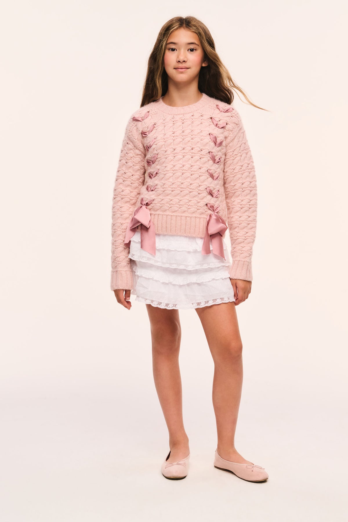 Tween pink textured knit pullover with ribbon threaded through the sides and bow at hem paired with a white mini skirt