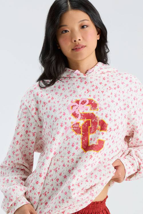 Pink floral hoodie close-up with hood and drawstring, gold-and-navy front graphic