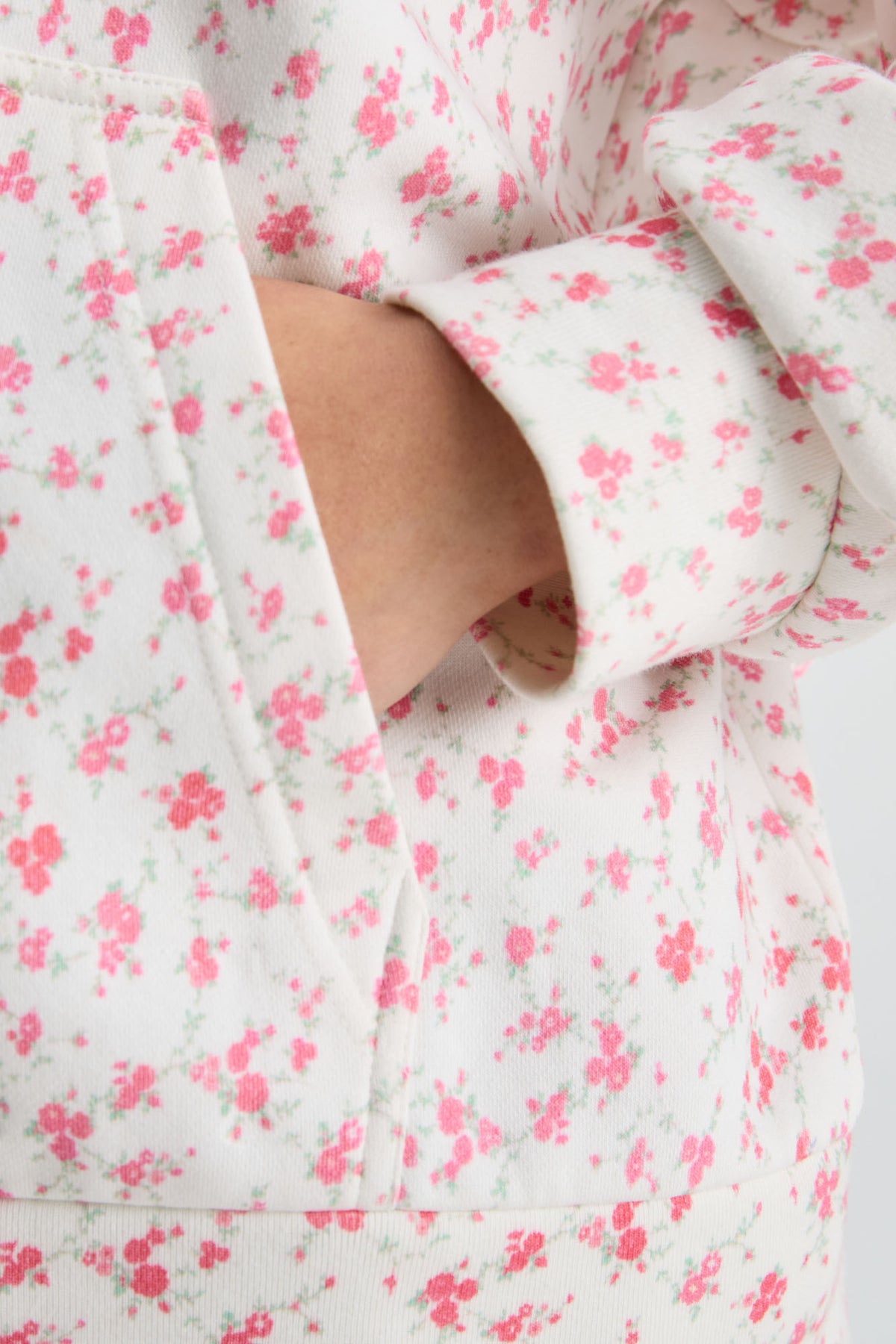 Pink floral hoodie close-up with kangaroo pocket and pink drawstring ends