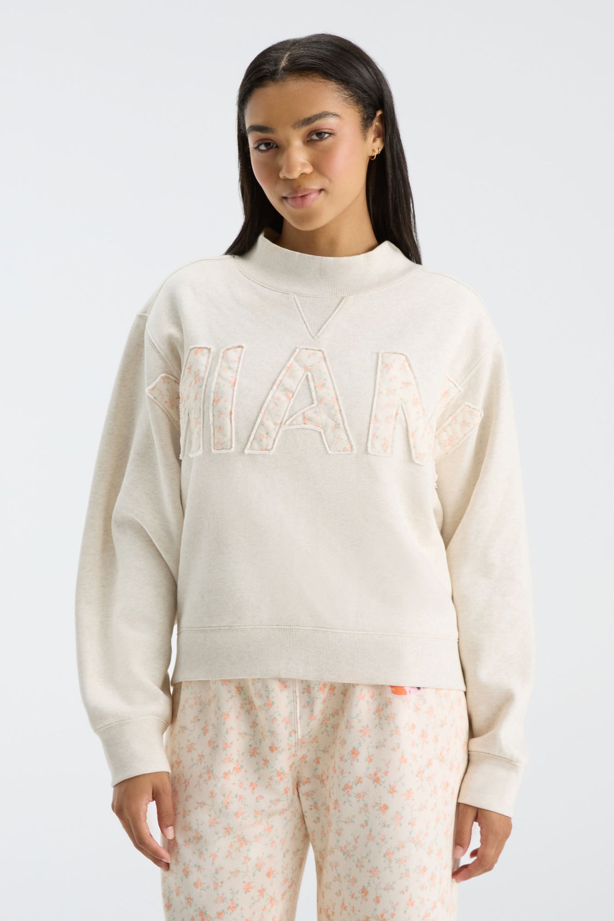 Front view: cream mockneck crew sweatshirt with oversized “FANATICS” floral letters