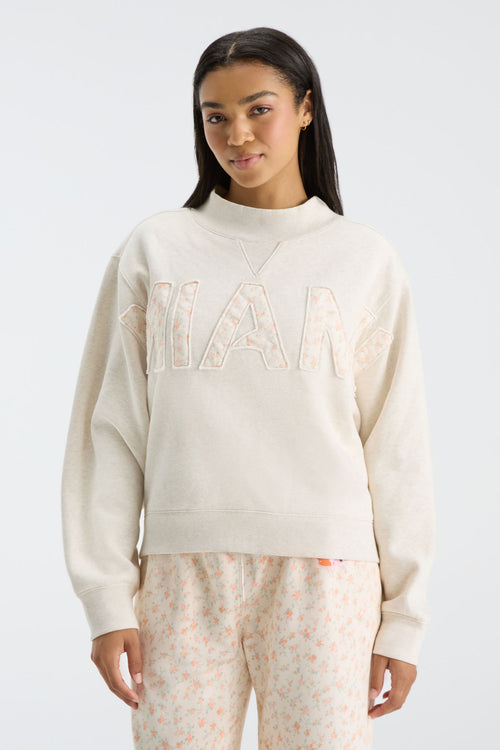 Front view: cream mockneck crew sweatshirt with oversized “FANATICS” floral letters