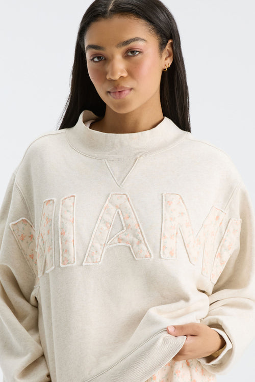 Close-up: cream mockneck crew sweatshirt showing “FANATICS” floral print letters