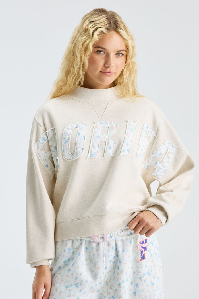Cream mockneck crew sweatshirt with raised letter graphic; styled with blue patterned set