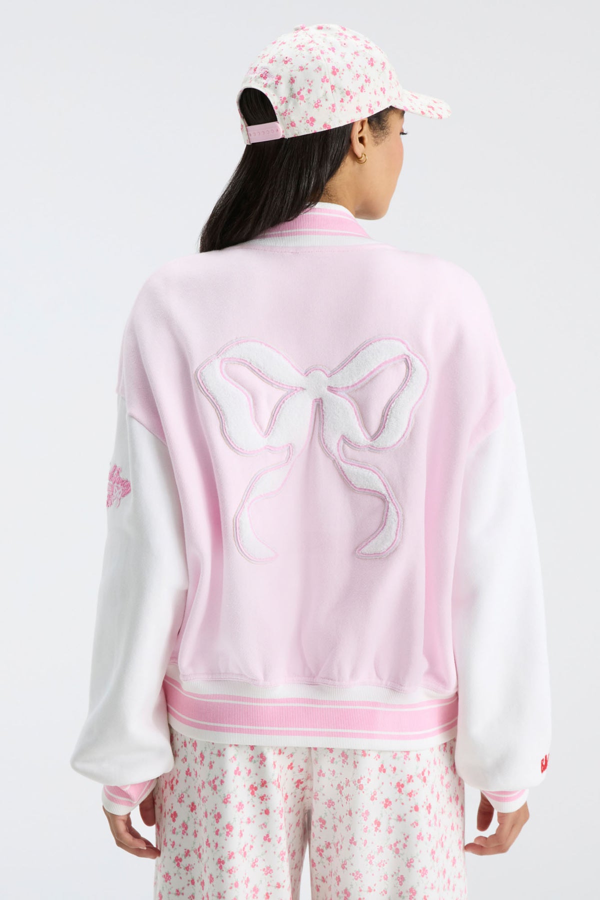 Light pink varsity jacket back with bow emblem and ribbed striped collar and hem.