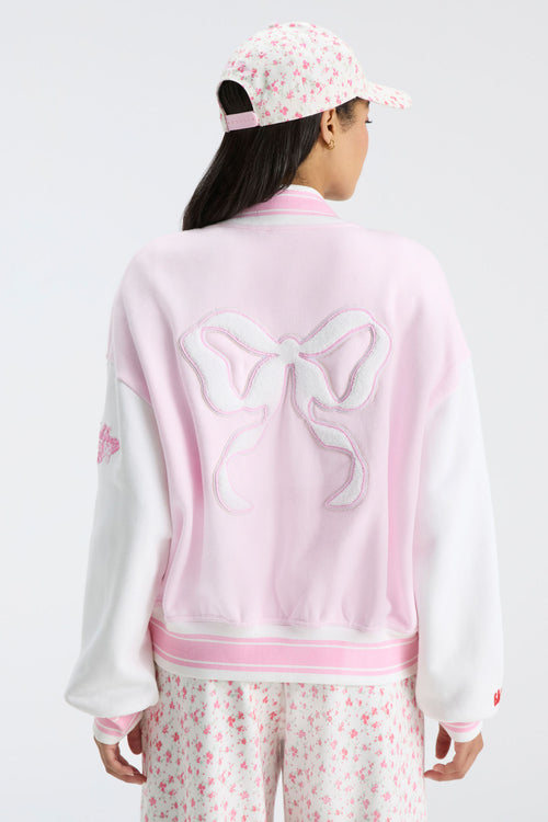 Light pink varsity jacket back with bow emblem and ribbed striped collar and hem.