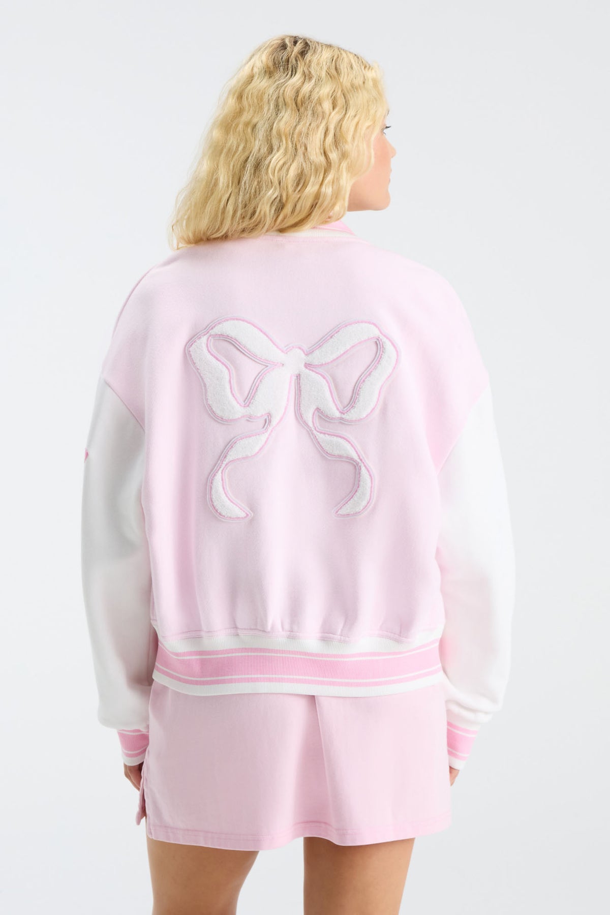 Pink back of varsity jacket with bow-like embroidered graphic and ribbed trim