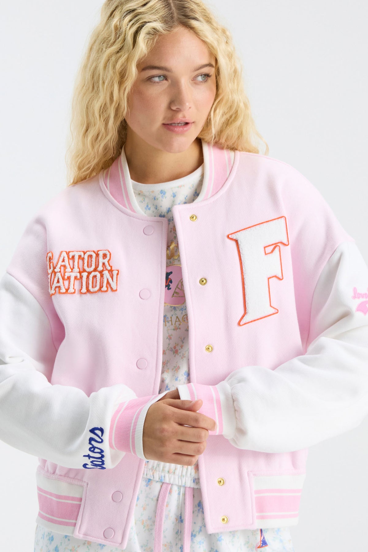 Light pink varsity jacket with orange logo patch, striped cuffs, and button front