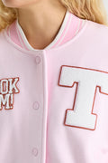 Light pink varsity jacket close-up with orange-outlined T patch and button placket