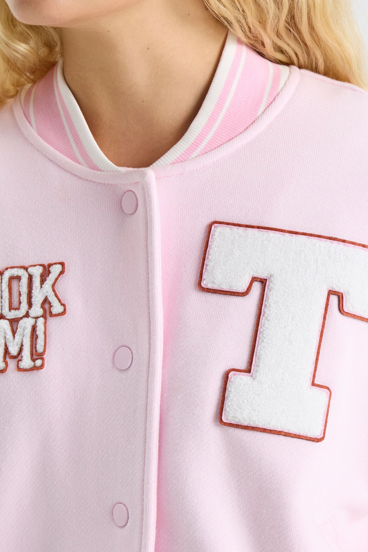 Light pink varsity jacket close-up with orange-outlined T patch and button placket