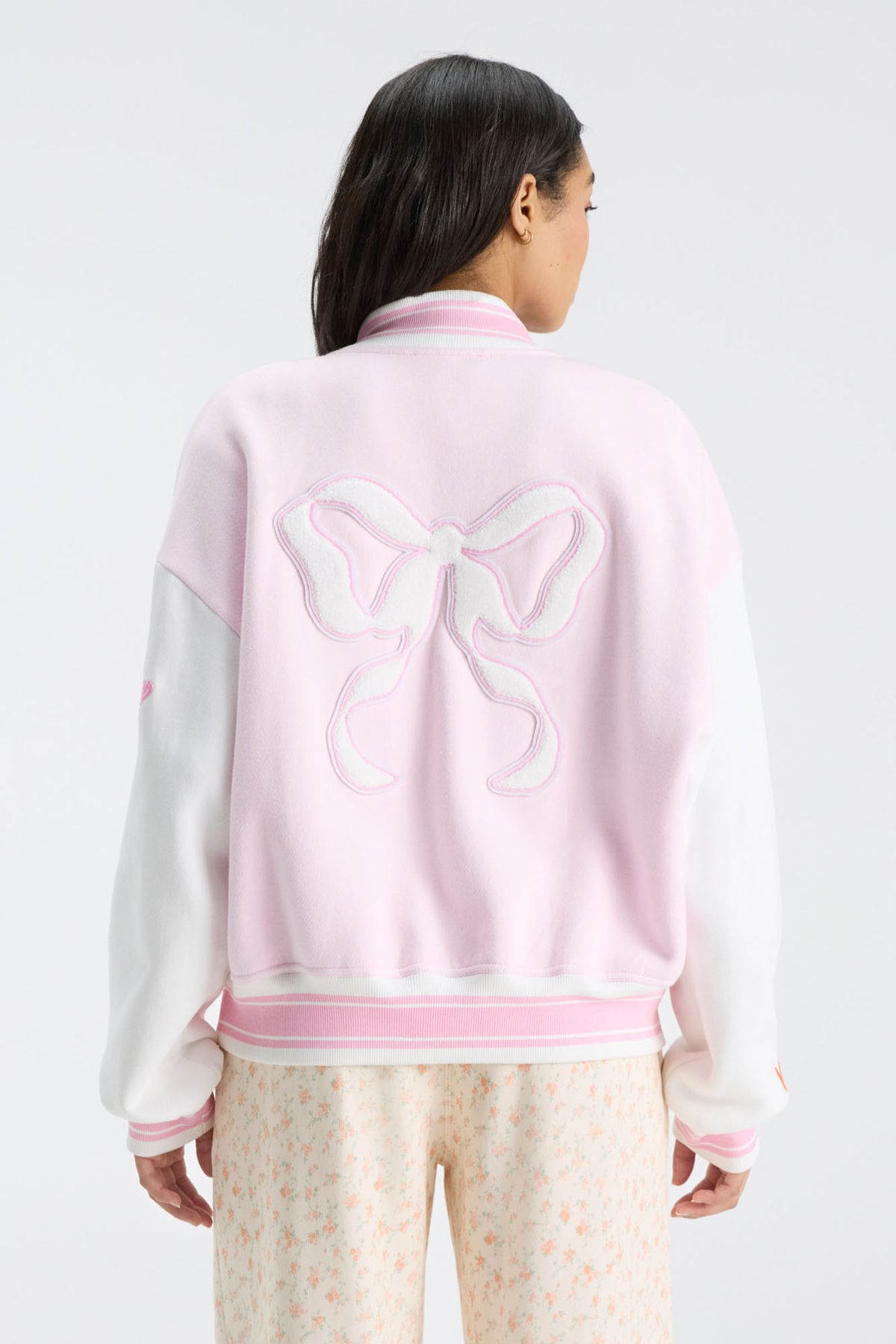 Pink varsity jacket with white sleeves and large bow graphic on the back.