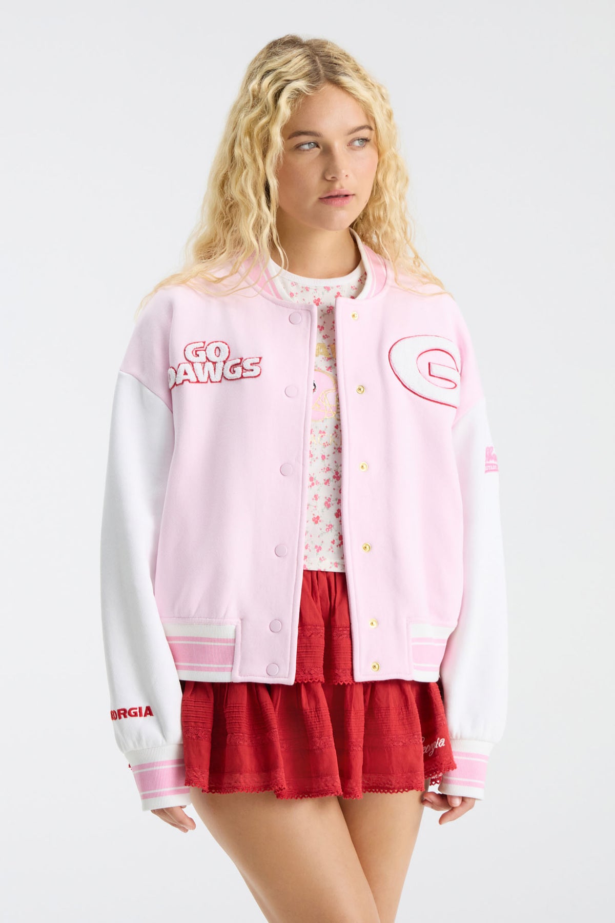 Pink varsity jacket with snap front and chest patches, paired with red skirt
