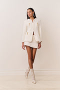 Cream tweed jacket worn with mini skirt, gold-tone charm accents and flap pockets