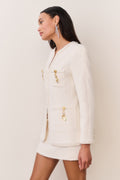 Cream tweed jacket with gold-tone embellishments, flap pockets, and fringe trim
