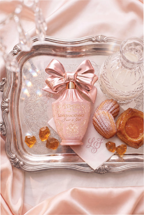 Close-up of pink perfume bottle with bow on a satin cloth with amber candies