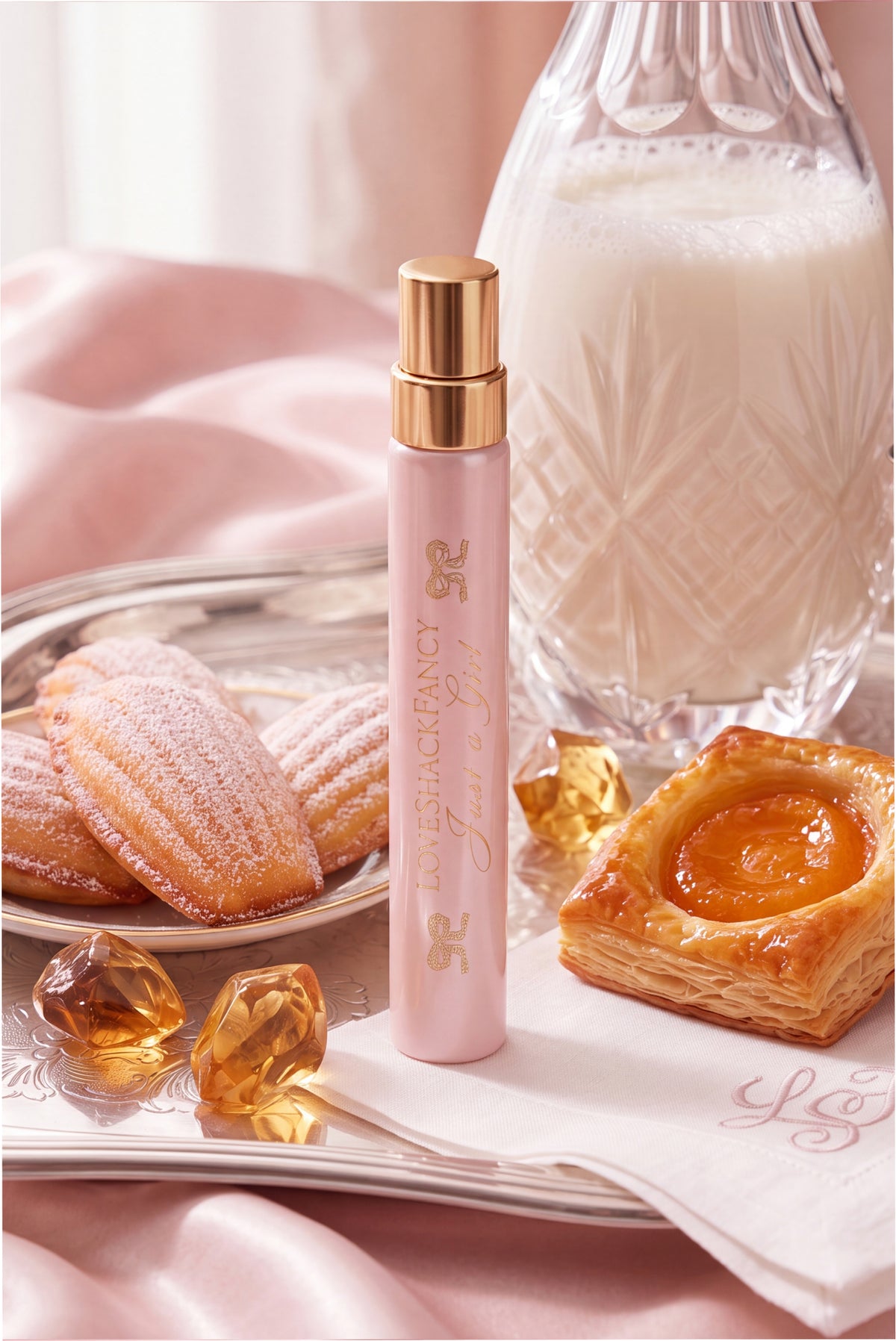 Pink perfume travel spray with gold cap on satin with macarons and pastry items.