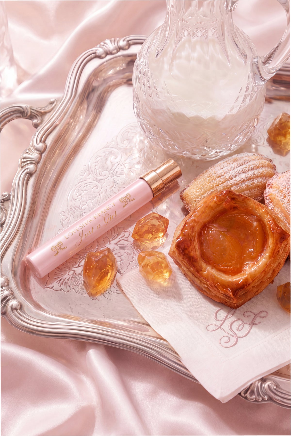 Close-up of pink perfume travel spray with gold cap on decorative tray and pastries.