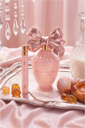 Pink bow perfume bottle with gold cap, shown on a tray with small gold candies