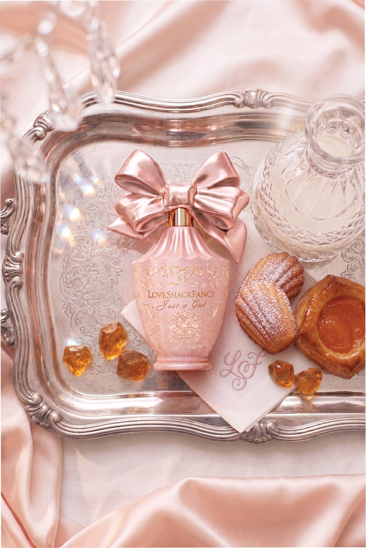 Pink bow perfume bottle on ornate tray with ribbon detail and amber-colored crystals