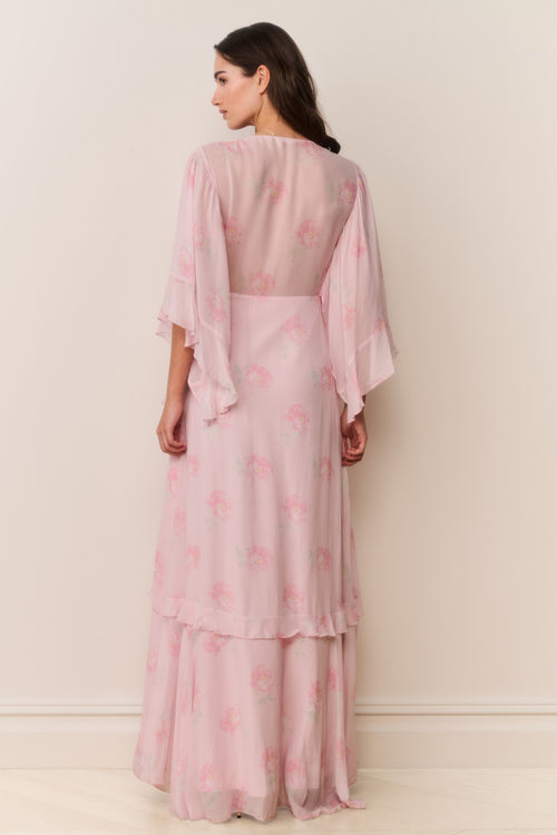 Woman wearing a pink floral dress with sheer sleeves against a white background