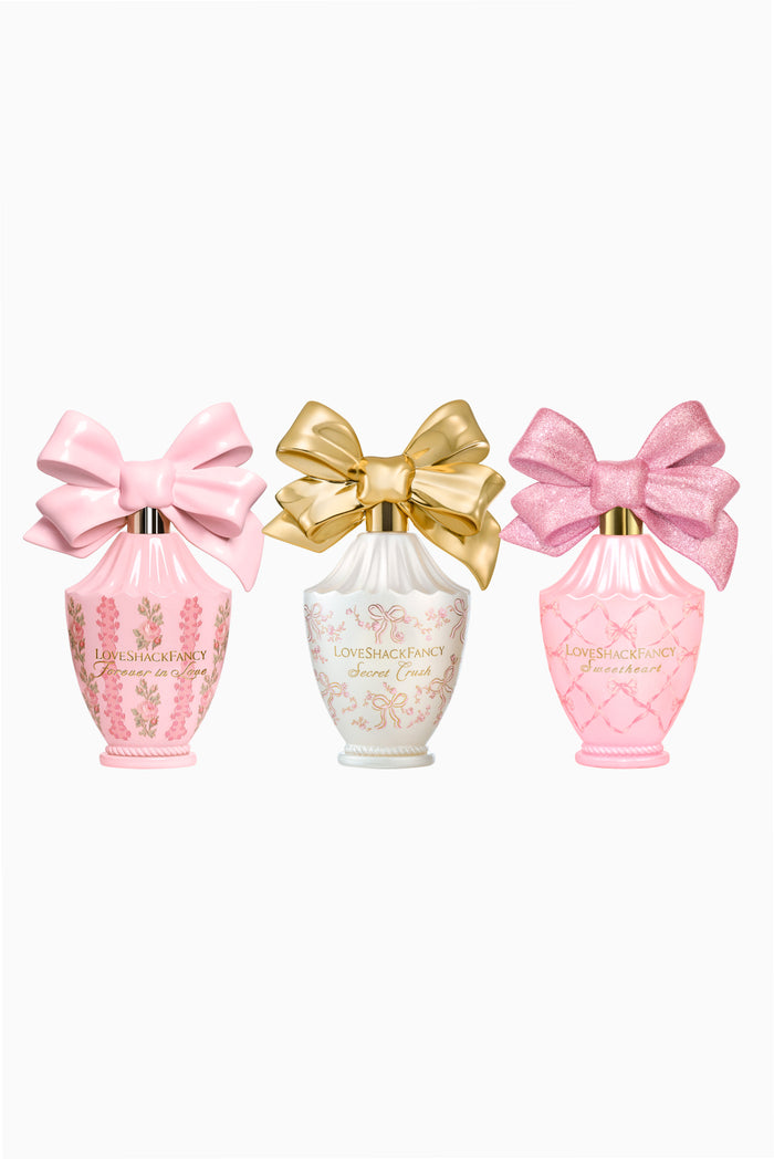 Three perfume bottles with pink and gold bows in pastel pink, gold, and white