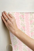 Hand applying peel-and-stick wallpaper with pink rose floral and green leaf pattern