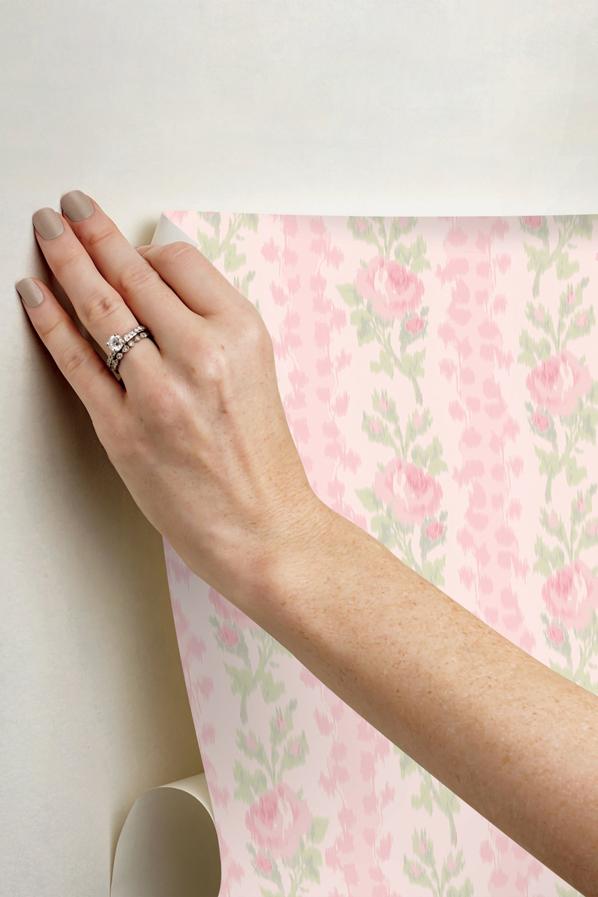 Hand applying peel-and-stick wallpaper with pink rose floral and green leaf pattern