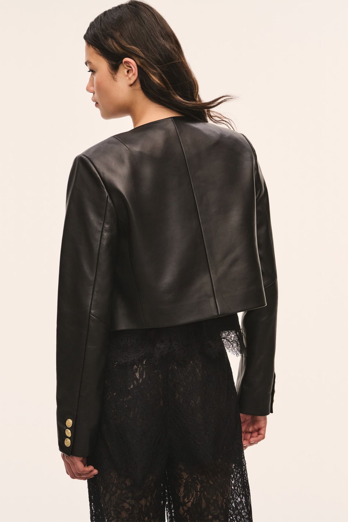 Back view of black collarless leather jacket with gold snap buttons and long sleeves