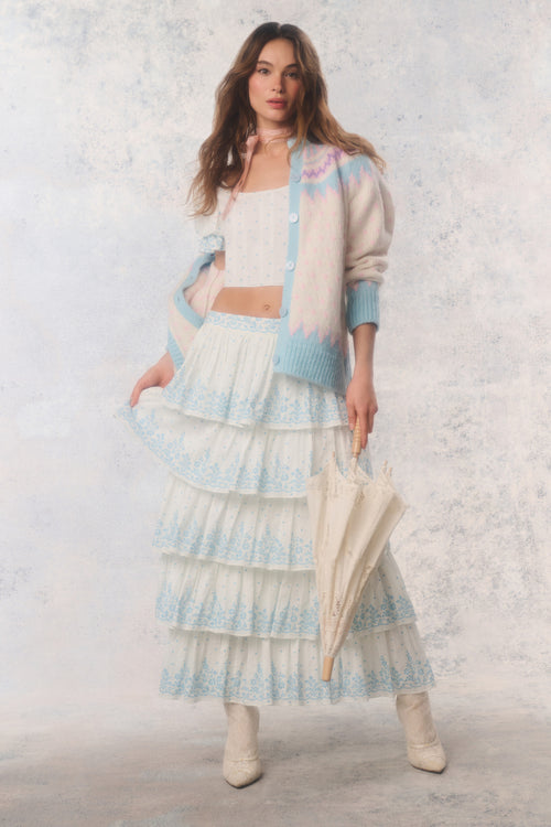 Woman wearing a pastel outfit with a cardigan and skirt against a light background