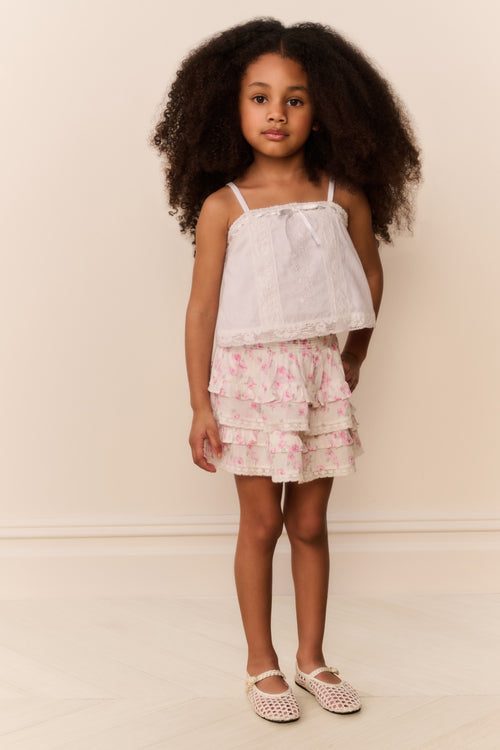 Young girl wearing a white top and floral ruffle skirt against a plain background