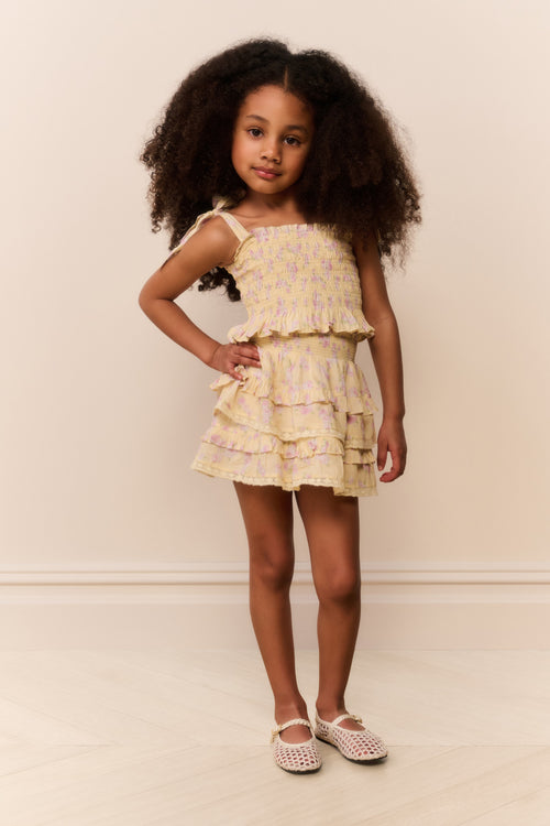 Young girl wearing a tiered yellow skirt with matching top with a neutral background