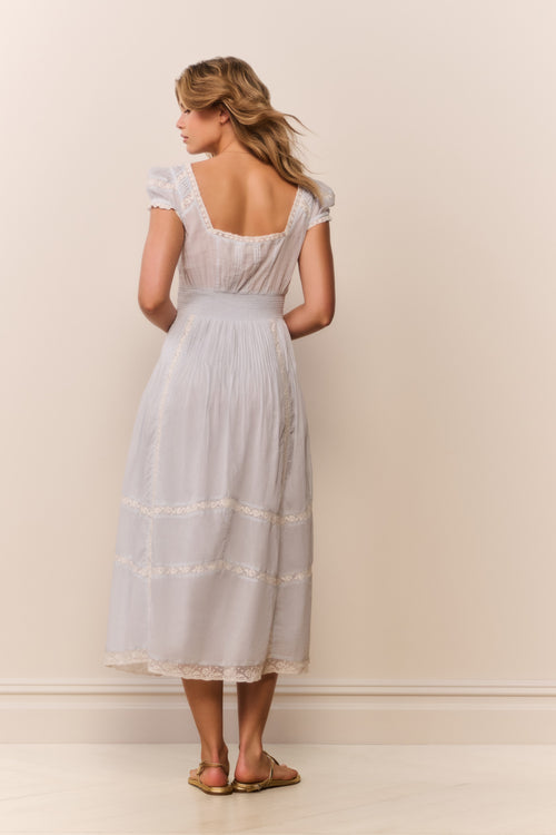 Woman wearing a light blue dress with lace details against a plain background