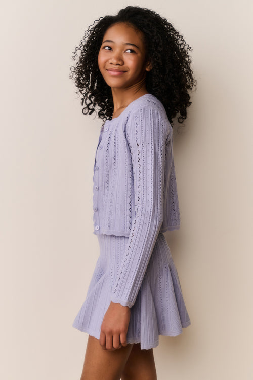 Young girl wearing a light purple knitted outfit against a beige background