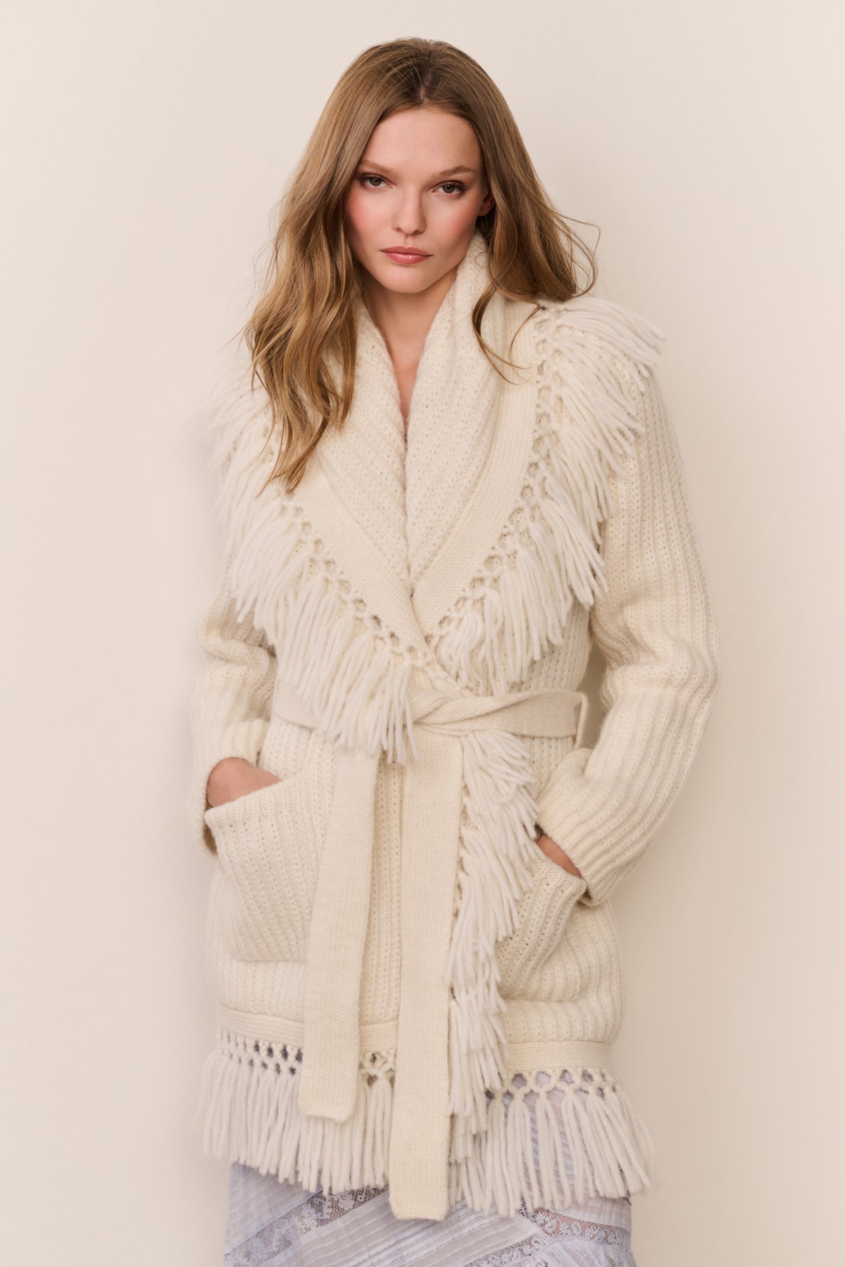 Ivory wrap cardigan with deep V neckline, fringe trim, and front patch pockets.