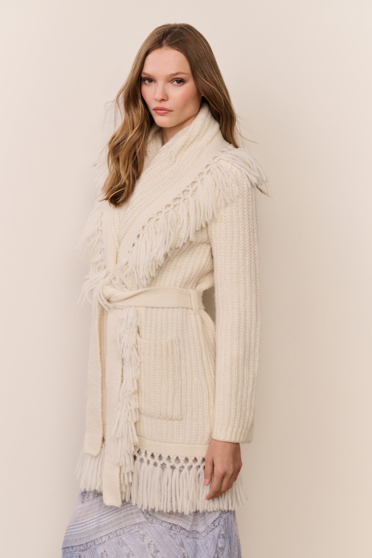 Ivory wrap cardigan with fringe shawl collar and tied waist, ribbed knit texture.