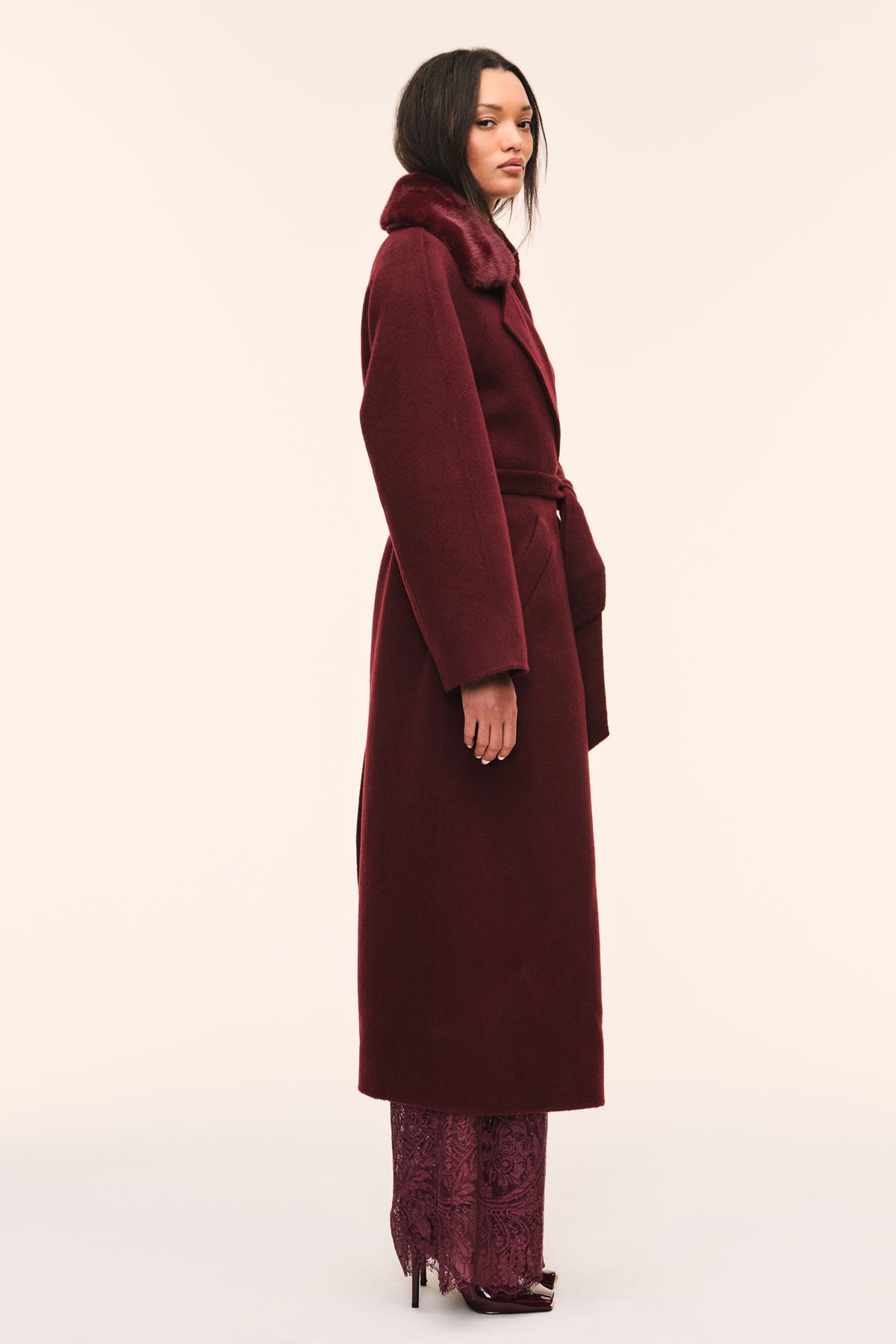 Side view of dark merlot faux fur collar wool coat with tied waist belt.