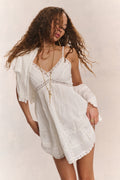 White cotton mini dress with spaghetti straps, lace V-neck, and tiered panels