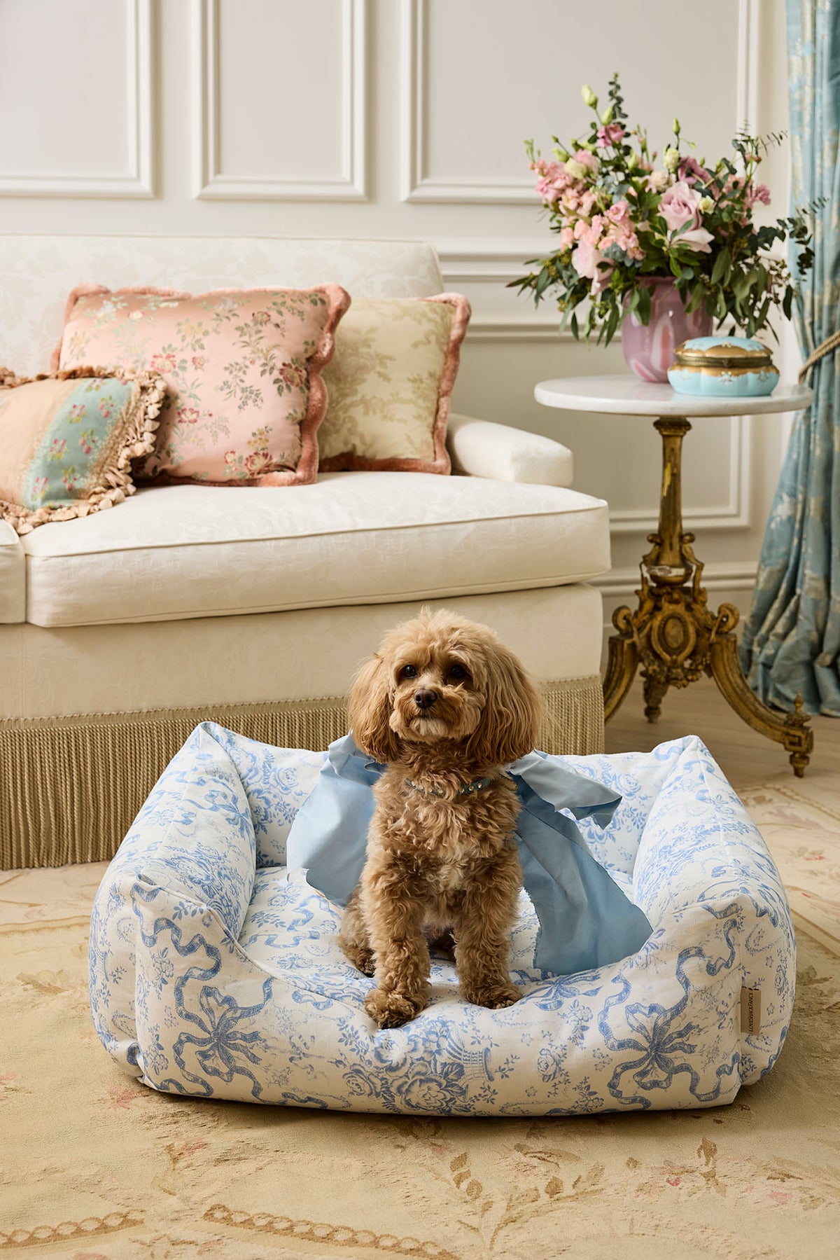 Printed dog bed with blue floral cover and small dog sitting on the cushion