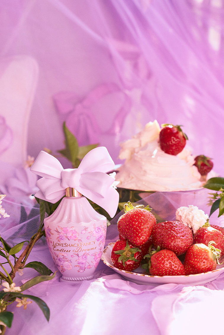 LoveShackFancy purple travel spray with white bow beside strawberries and flowers