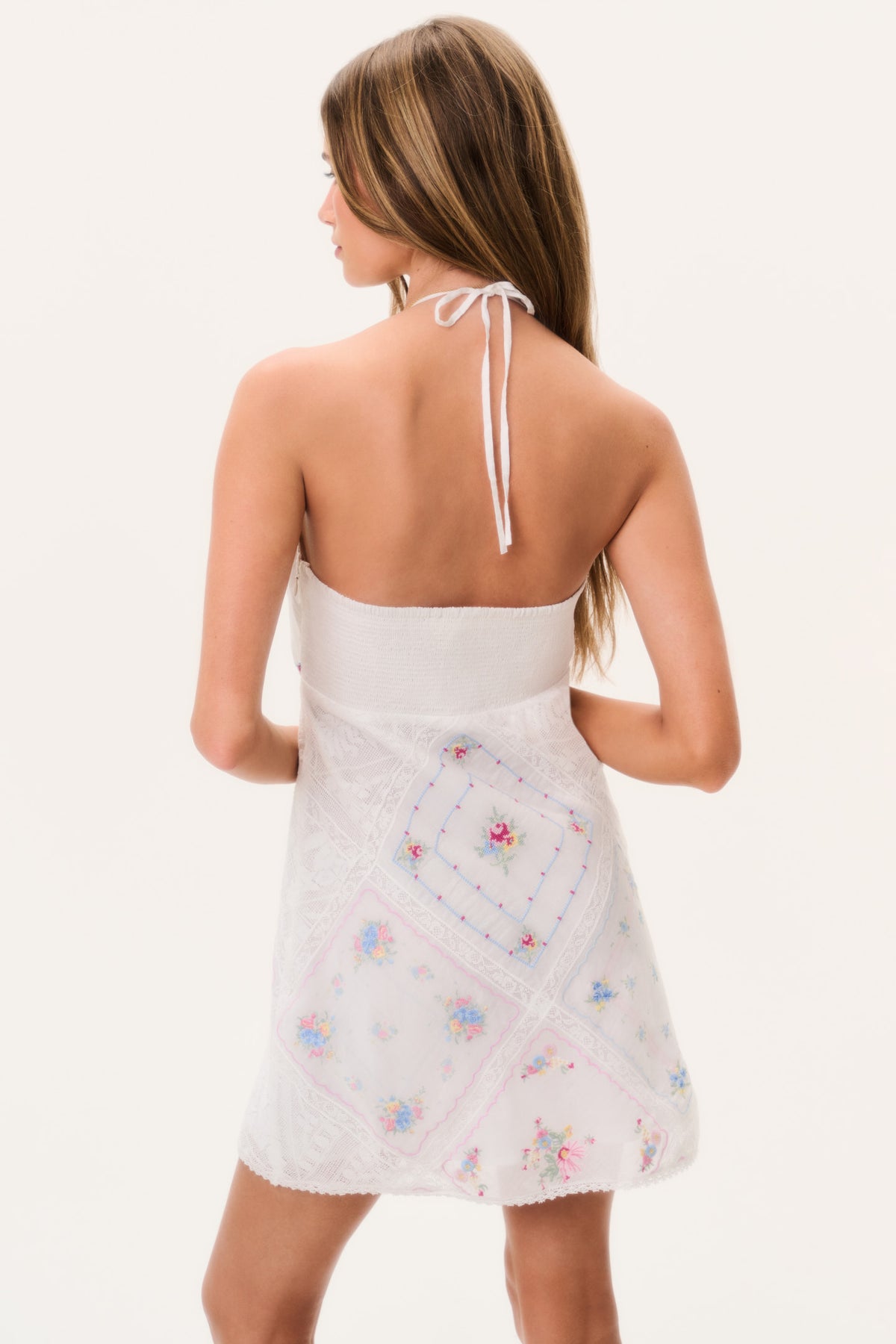 Back view of white embroidered patchwork mini dress with adjustable tie straps