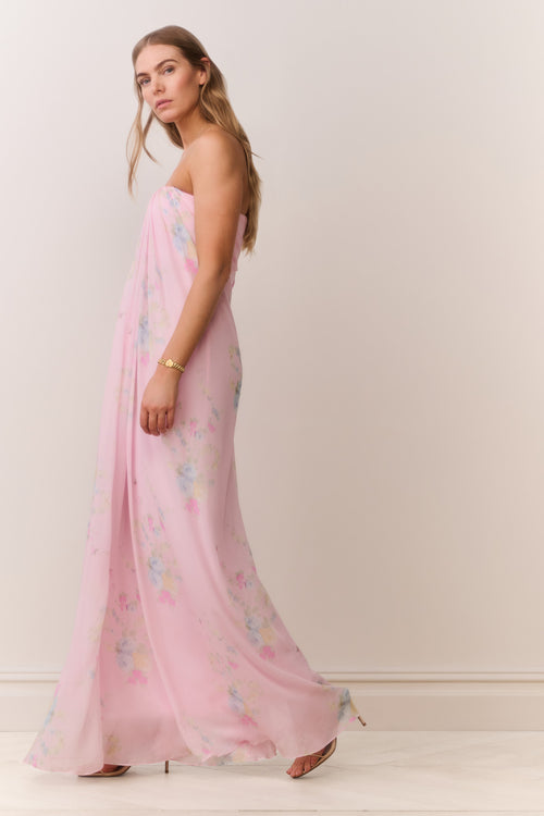 Woman wearing a pink strapless dress with floral patterns on a plain background