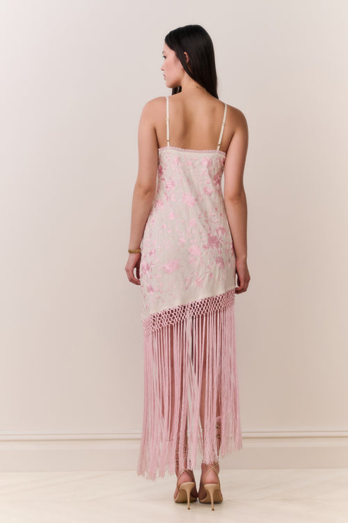 Woman wearing a pink floral dress with fringe hemline details on a plain background