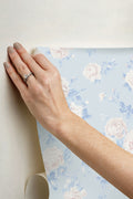 Whisper blue peel-and-stick wallpaper being applied by hand; floral pattern