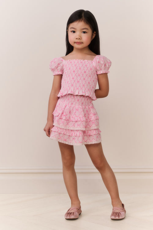 Young girl wearing a pink patterned ruffled top and matching skirt against a plain background