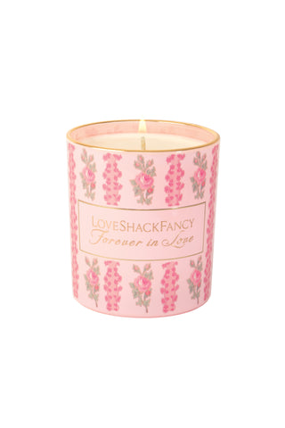 Pink floral scented candle in glass with centered wick flame and printed label