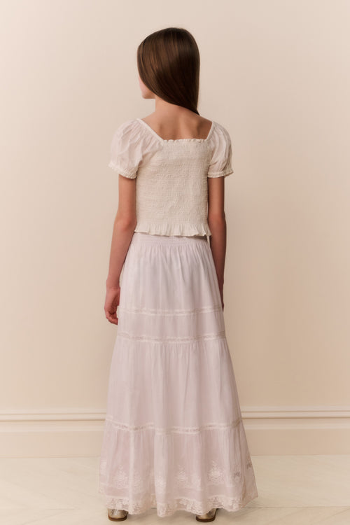 Girl wearing a white lace top and long skirt against a plain background