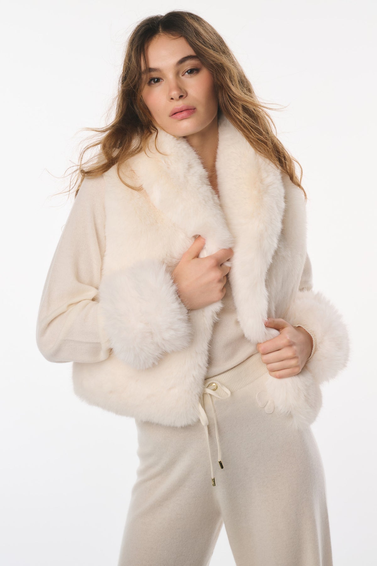 Ivory faux fur vest worn open with plush trim along armholes and front