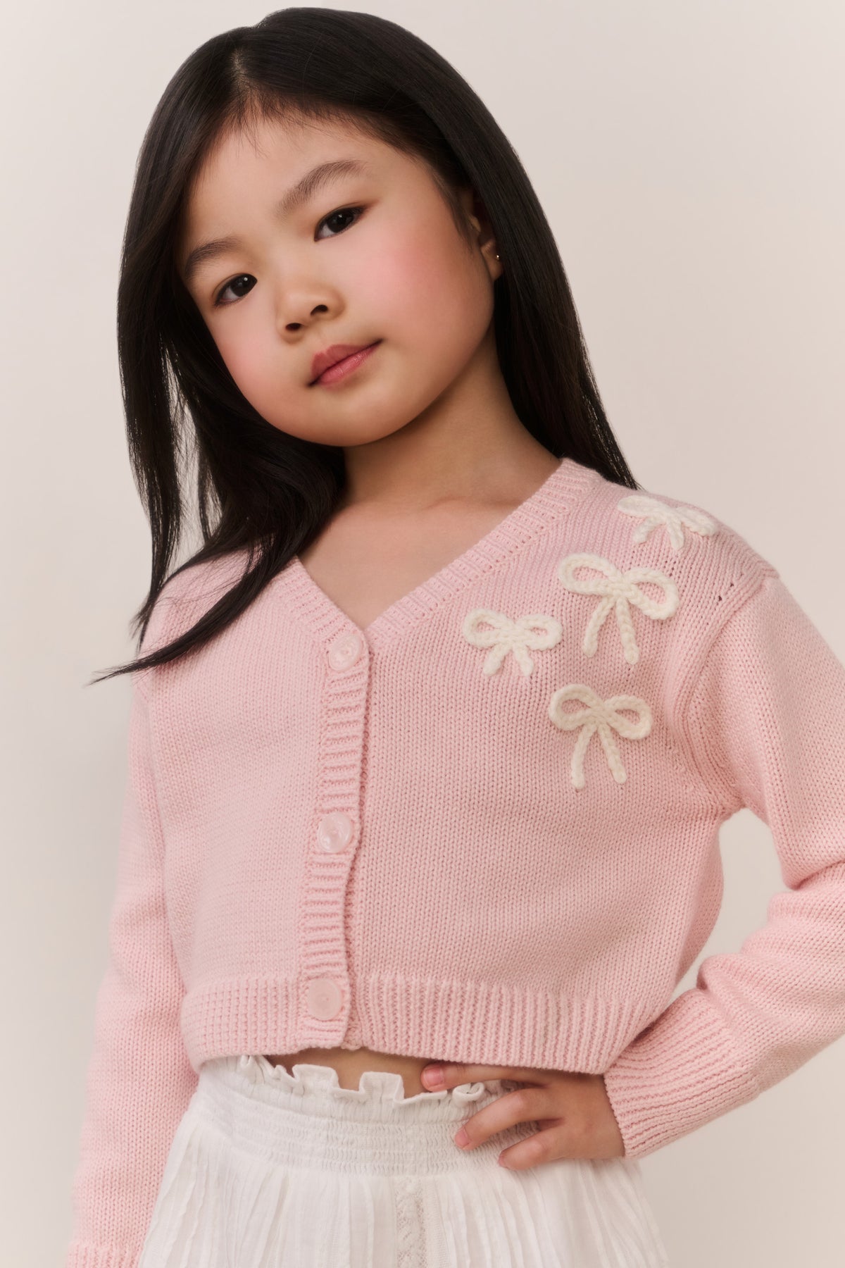 Girls pink cardigan close-up with bow embroidery on shoulders and button placket