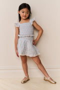 Girls floral cotton mini skirt angled front view; light ivory with gathered waist and ruffles